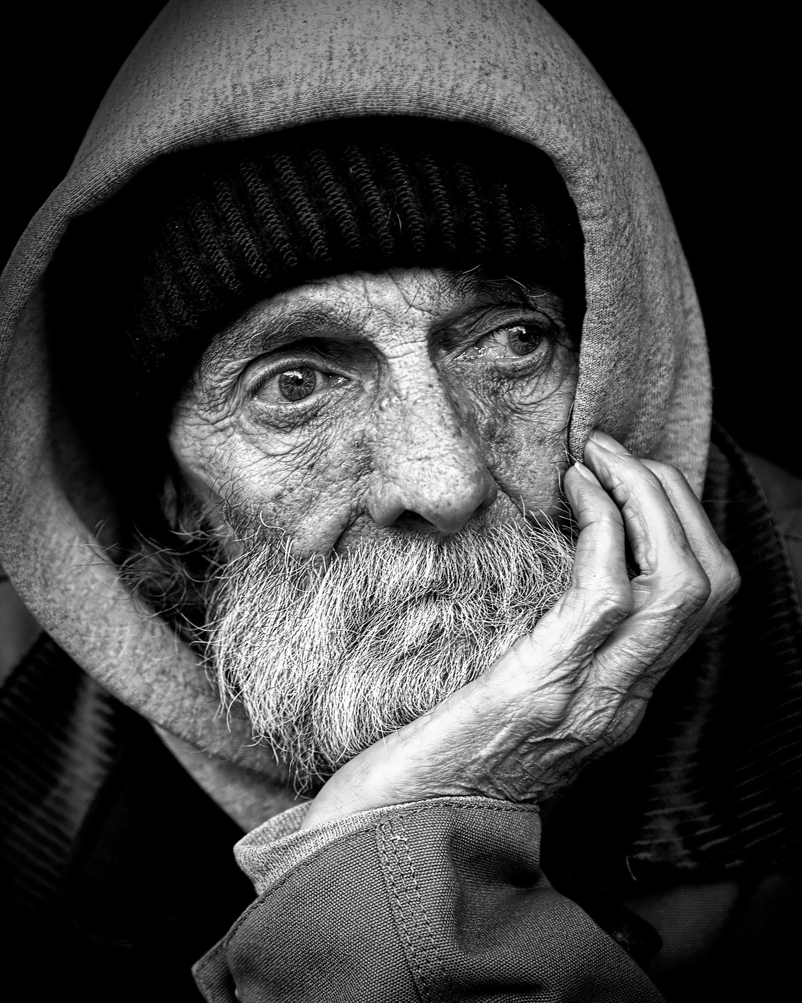 Black and white portrait of an elderly man with a thoughtful expression, wearing a hood.