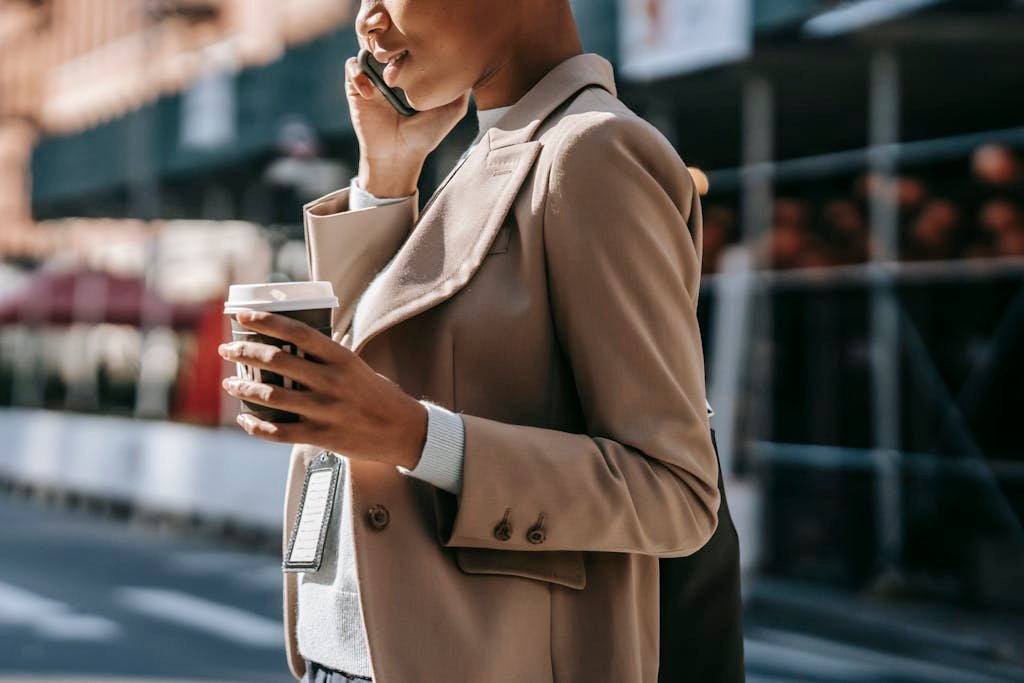 Side view of a young African American businesswoman talking on the phone with a takeaway coffee, walking outdoors.